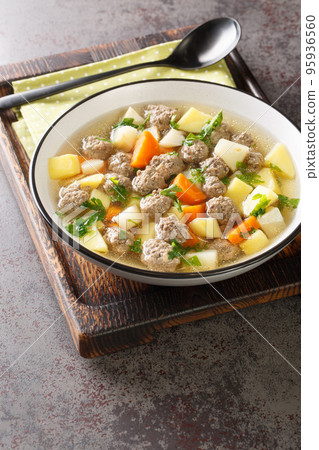 Sodd is a traditional Norwegian soup made with cooked mutton and meatballs and potatoes, carrots are included in a clear, fragrant broth closeup in the plate. Vertical 95936560