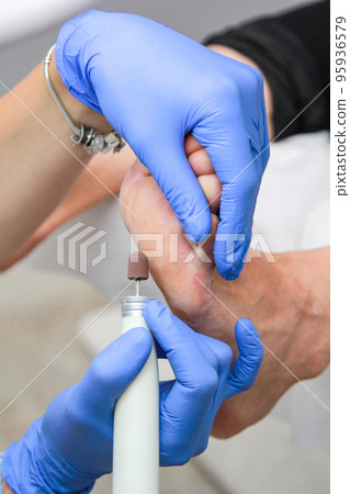 A pedicure master treats the heel with a power tool in a beauty salon. A pedicure master treats the heel with a power tool in a beauty salon. 95936579