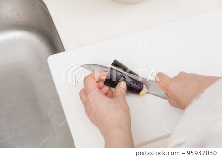 [A middle-aged housewife cuts an eggplant into strips with a Santoku knife] 95937030