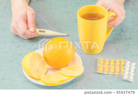 Sick person who is looking at thermometer and drinking hot tea with lemon 95937479