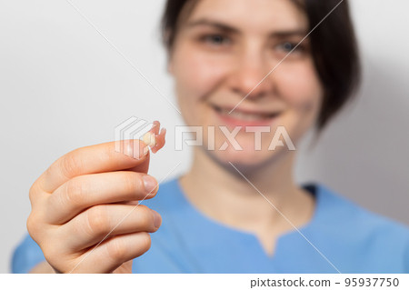 Dentist holding ceramic artificial false unit tooth. Dental prosthesis in gloved hands of the doctor close-up. Dentistry conceptual photo. Prosthetic dentistry. False teeth Dentist holding ceramic artificial false unit tooth. Dental prosthesis in gloved hands of the doctor close-up. Dentistry conceptual photo. Prosthetic dentistry. False teeth 95937750