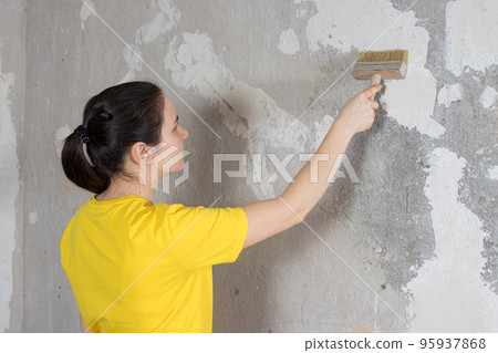 A woman repairman puts wallpaper glue on the wall. The wallpaper in the house and repair with their own hands yourself 95937868