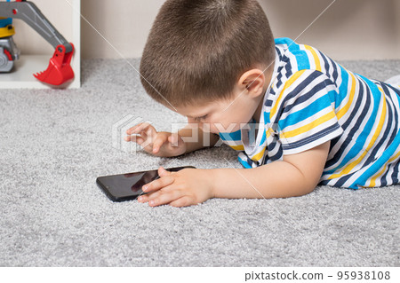 A little boy 3-4 years old looks into the phone screen. Cartoons for children, screen time, children's dependence on the computer and phone A little boy 3-4 years old looks into the phone screen. Cartoons for children, screen time, children's dependence on the computer and phone 95938108