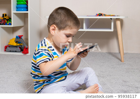 A small child and a mobile phone in the children's room with place for text. Cartoons and dependence on gadgets in children, limiting children from adult content on the Internet 95938117
