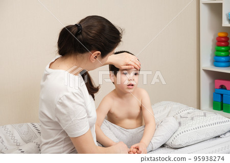 The mother measures the temperature of a sick child, puts her hand to her forehead. Illnesses with fever in children, influenza or coronavirus 95938274