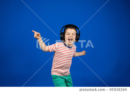 Happy smart 5 year old boy in big black headphones points fingers to the sides in place for text copy space 95938384