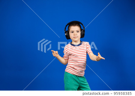 Happy smart 5 year old boy in big black headphones points fingers to the sides in place for text copy space Happy smart 5 year old boy in big black headphones points fingers to the sides in place for text copy space 95938385