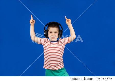 Happy boy in headphones and t-shirt points his fingers up on a blue background Happy boy in headphones and t-shirt points his fingers up on a blue background 95938386