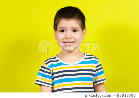 Portrait of a smiling handsome brunette boy of 4 years old in a striped blue T-shirt on a yellow background, copy the place for the text 95938396