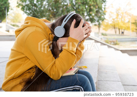Sad teenage girl in headphones will cover her face with her hands, a place for text 95938723