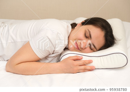 A woman sleeps on her stomach on an orthopedic pillow made of memory foam. A woman sleeps on her stomach on an orthopedic pillow made of memory foam. 95938780