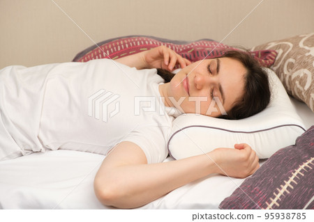 A woman lies on an orthopedic pillow, choosing it among other different pillows A woman lies on an orthopedic pillow, choosing it among other different pillows 95938785