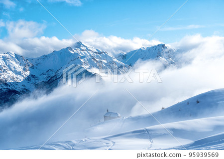 Snow covered mountain peaks above the clouds. High mountains in winter landscape. Briancon one of largest ski resort in Europe. View of the ski area and house with nobody around. . 95939569
