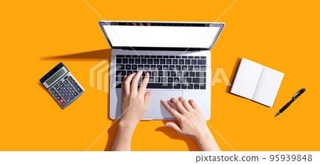 Person using a laptop computer with a notebook and a calculator Person using a laptop computer with a notebook and a calculator 95939848