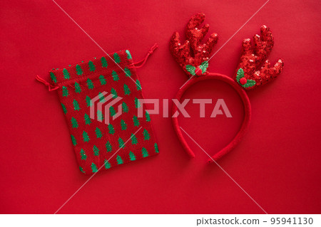 Christmas accessories, deer antlers headband on red glitter surface and gift bag, greeting card. Minimal winter holidays idea. Flat lay top view 95941130