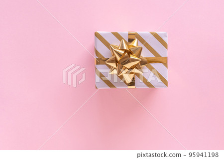 Christmas giftbox with golden ribbon on pastel pink surface. Holiday present. Festive greeting card. Top view 95941198
