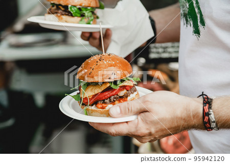 Man holds in his hand burgers at a burger feast. Dinner Hamburger Food Feast Party. Big burger in 95942120