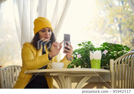 Stylish woman using mobile phone while a coffee break in a cafe. Reading news, social network, surfing the internet, scrolling newsfeed, checking content in social media in smartphone. Coffee break Stylish woman using mobile phone while a coffee break in a cafe. Reading news, social network, surfing the internet, scrolling newsfeed, checking content in social media in smartphone. Coffee break 95942517