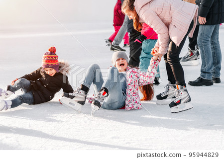 Soft,Selective focus.A kid takes relax after his fall while skating.People, friendship, sport and leisure concept - happy friends on skating rink.Group of teenage friends ice skating on an ice rink. Soft,Selective focus.A kid takes relax after his fall while skating.People, friendship, sport and leisure concept - happy friends on skating rink.Group of teenage friends ice skating on an ice rink. 95944829