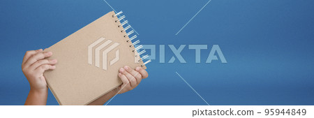 Notepad in hand. Blank notepad in the hands of a child on a blue background. Hands hold a book without text. The girl is holding a book with an empty cover. 95944849