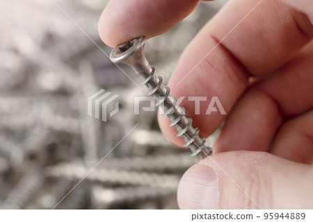 A man holds a screw, close-up. Screws for the production of wooden furniture. Repair and repair tools. Stainless steel bolts. 95944889