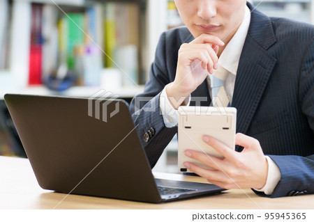 A businessman who worries while looking at a calculator A businessman who worries while looking at a calculator 95945365