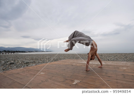 Shirtless caucasian man doing backflip on pebble beach.  95949854