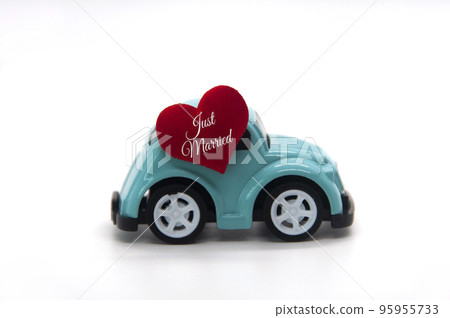 Mini toy car carrying red heart shape with text Just Married. Newly wed couple concept. Mini toy car carrying red heart shape with text Just Married. Newly wed couple concept. 95955733