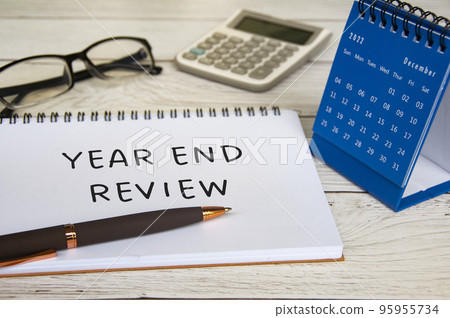 Year end review text on notepad with December calendar, glasses, calculator and pen. Year end review concept. Year end review text on notepad with December calendar, glasses, calculator and pen. Year end review concept. 95955734