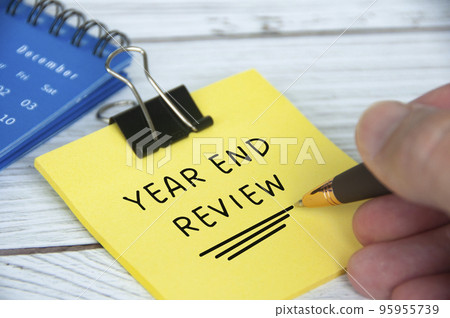 Year end review text on yellow notepad with December calendar background. Year end closing and review concept. Year end review text on yellow notepad with December calendar background. Year end closing and review concept. 95955739