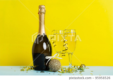 Champagne bottle with confetti, glasses and christmas decor on colored holiday background. Flat lay New Year decorations Champagne bottle with confetti, glasses and christmas decor on colored holiday background. Flat lay New Year decorations 95958526