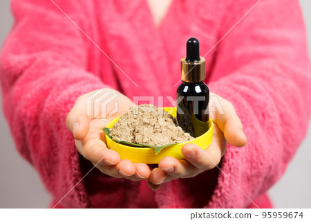 A woman in a pink robe keeps natural cosmetics for facial skin care - ubtan and oil 95959674
