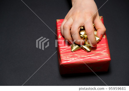 A woman's hand grabs a gift box by a bow on a black background with a place for text. A woman's hand grabs a gift box by a bow on a black background with a place for text. 95959681