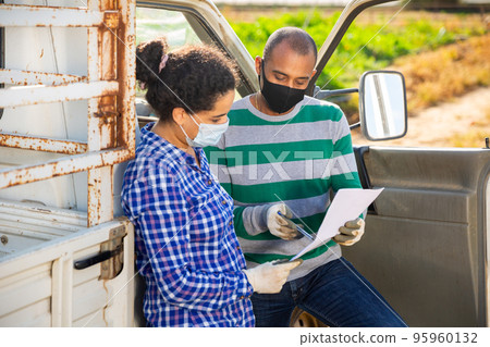 Delivery courier in protective masks invites the farmer to sign documents on the field Delivery courier in protective masks invites the farmer to sign documents on the field 95960132