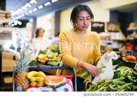 Hispanic woman putting green beans in plastic bag in store Hispanic woman putting green beans in plastic bag in store 95960294