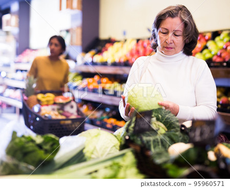 Mature woman choice cabbage on grocery store shelves 95960571