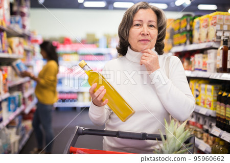 Pensive elderly woman choosing vegetable oil in supermarket Pensive elderly woman choosing vegetable oil in supermarket 95960662