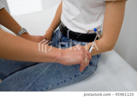 Neurological examination. Neurologist checks reflexes on a female patient arm using a hammer 95961120
