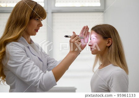 Female doctor checking young female patient's eyes with fashlight. .Diagnosis of neurological diseases Female doctor checking young female patient's eyes with fashlight. .Diagnosis of neurological diseases 95961133