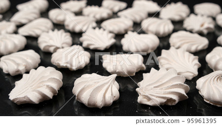 White meringues on a black background, sweet pastries, a dessert of sugar and egg white. White meringues on a black background, sweet pastries, a dessert of sugar and egg white. 95961395