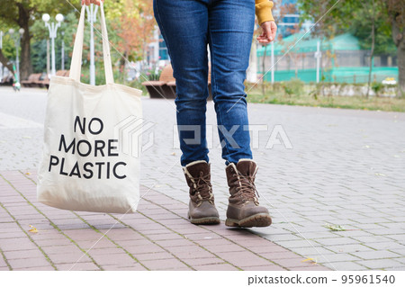 Human feet in boots and a reusable cloth bag with the inscription No more plastic 95961540