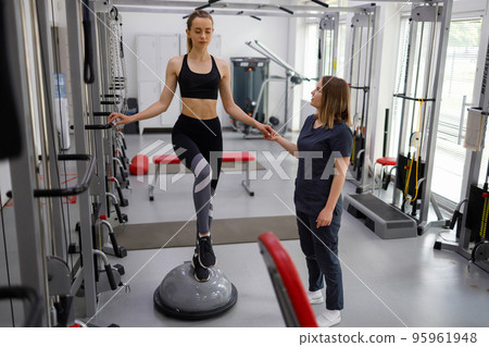 Physiotherapist helping female patient with rehabilitation. Balance exercise with bosu ball. Woman and doctor during rehab physiotherapy in gym Physiotherapist helping female patient with rehabilitation. Balance exercise with bosu ball. Woman and doctor during rehab physiotherapy in gym 95961948