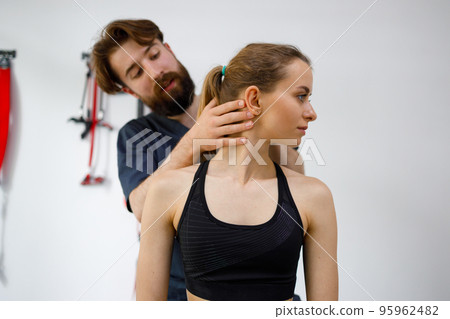 Focused male manual therapist turning head of female patient to check his injured neck. Concept of exercises with the diagnosis of diseases of the cervical spine Focused male manual therapist turning head of female patient to check his injured neck. Concept of exercises with the diagnosis of diseases of the cervical spine 95962482