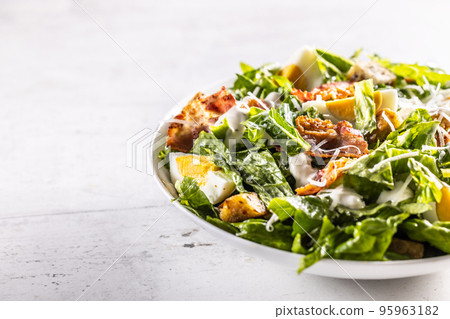 Caesar salad prepared from romaine lettuce, baked bacon, egg, bread croutons, garlic dressing and grated Parmesan cheese. 95963182