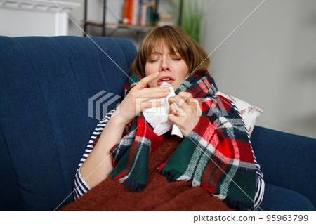 Sick woman with a runny nose lying on a sofa under a blanket with a handkerchief 95963799