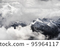 A landscape of the Dolomites Mountain Range covered in the fog under a cloudy sky in Italy 95964117
