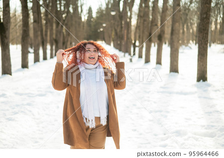 A fat woman listens to music with headphones and dances in the park in winter.  95964466