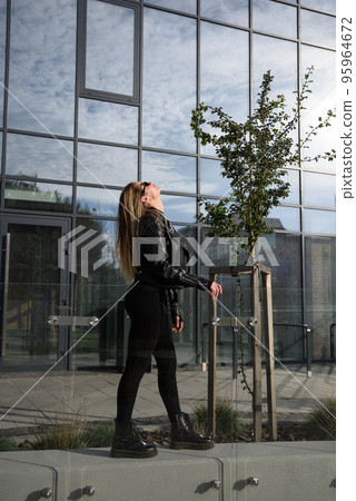 Fashionable young woman with long hair wearing solid long sleeve bodycon one piece jumpsuits posing in a black leather jacket and smooth platform boots Fashionable young woman with long hair wearing solid long sleeve bodycon one piece jumpsuits posing in a black leather jacket and smooth platform boots 95964672