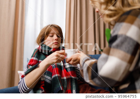 Mother gives a mug of hot tea to her daughter who is sick with the flu 95964755