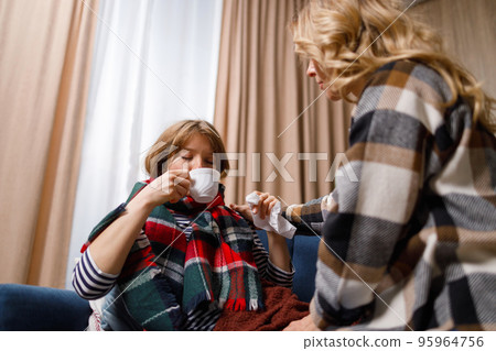 Mother gives a mug of hot tea to her daughter who is sick with the flu. Woman caring for her daughter who has a cold Mother gives a mug of hot tea to her daughter who is sick with the flu. Woman caring for her daughter who has a cold 95964756